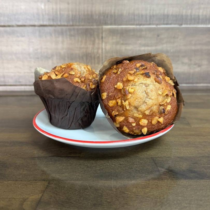 Two golden-brown muffins with nut toppings in dark wrappers, on a white plate with a red rim.