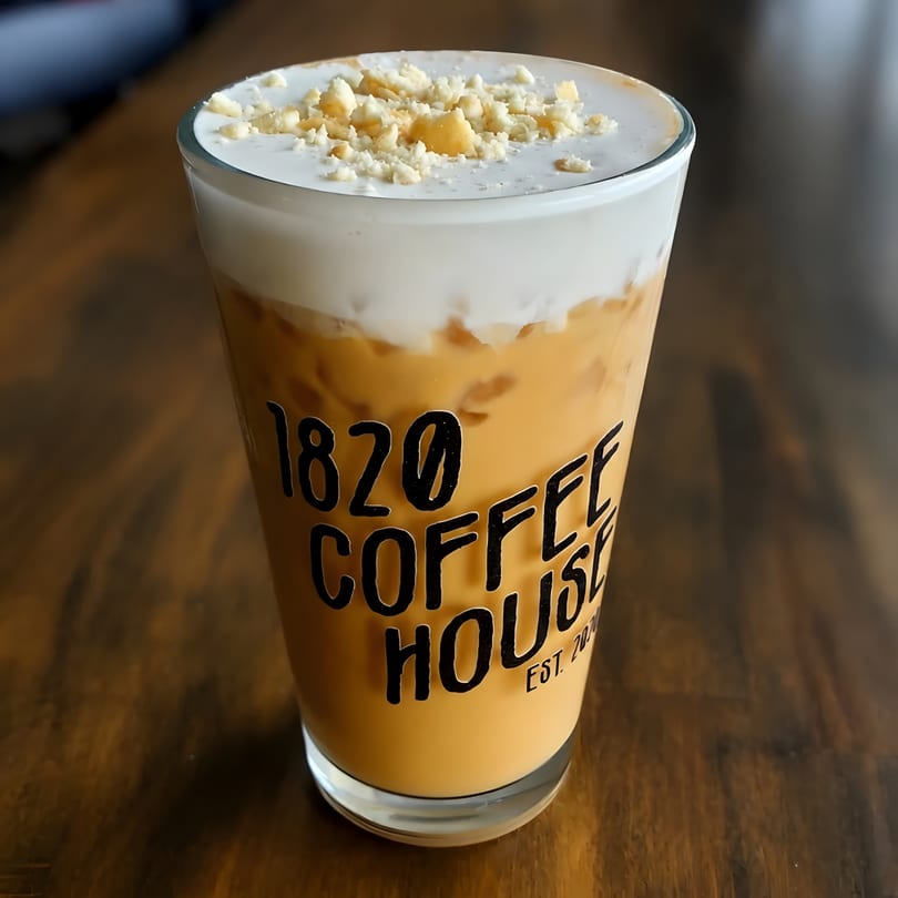 Iced coffee with a creamy foam top and crushed nuts, in a glass from 1820 Coffee House.