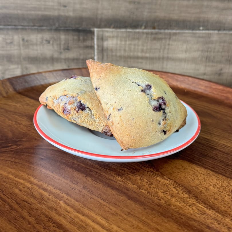 Two golden-brown blueberry scones with visible berries, on a white plate with a red rim.