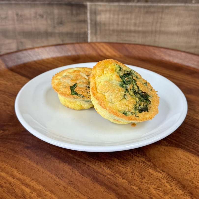 Two golden-brown spinach and cheese quiches on a white plate, on a wooden table.